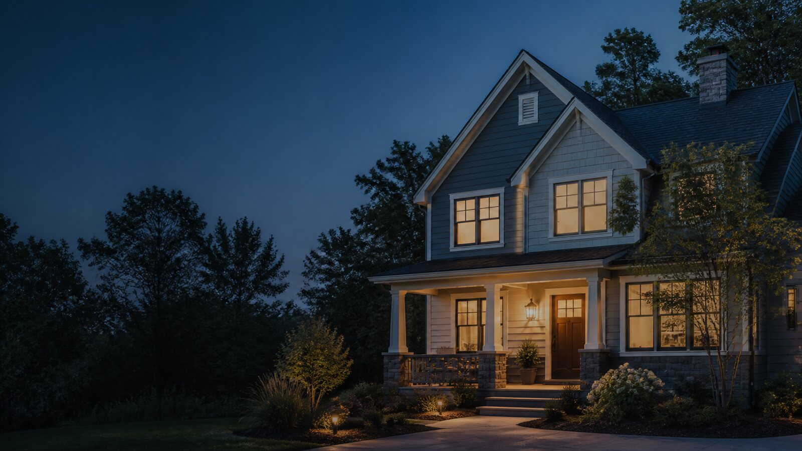 A two-storey house at dusk with its porch and windows lit